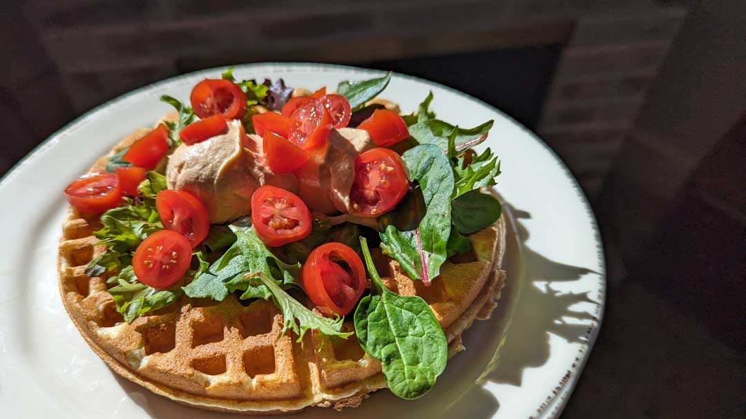waffle topped with mixed greens, tomatoes, and hummus
