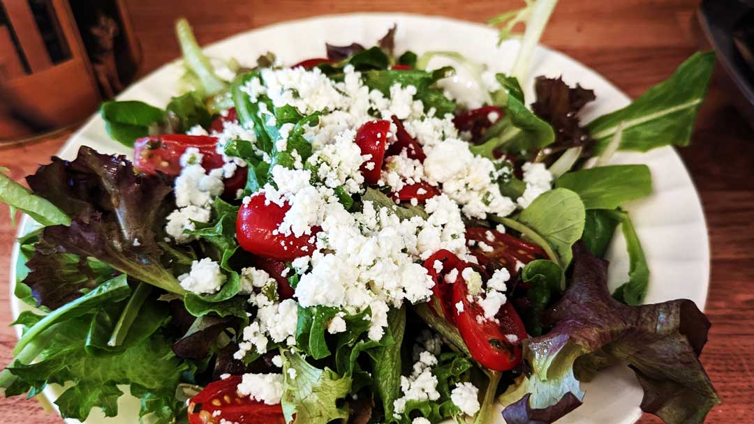 Mixed greens with tomatoes and feta on white plate